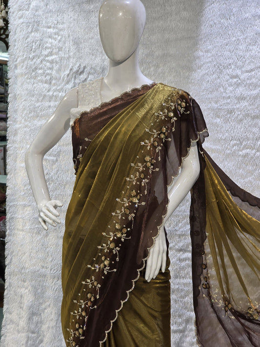 This premium copper pure satin silk saree features a stylish plain body complemented by a beautifully crafted border with floral stone work and tikali detailing. The added necklace border design enhances its regal appeal. Paired with a contrast chocolate-brown blouse, this saree carries a sophisticated modern-traditional blend, perfect for festive occasions and elegant evening wear.