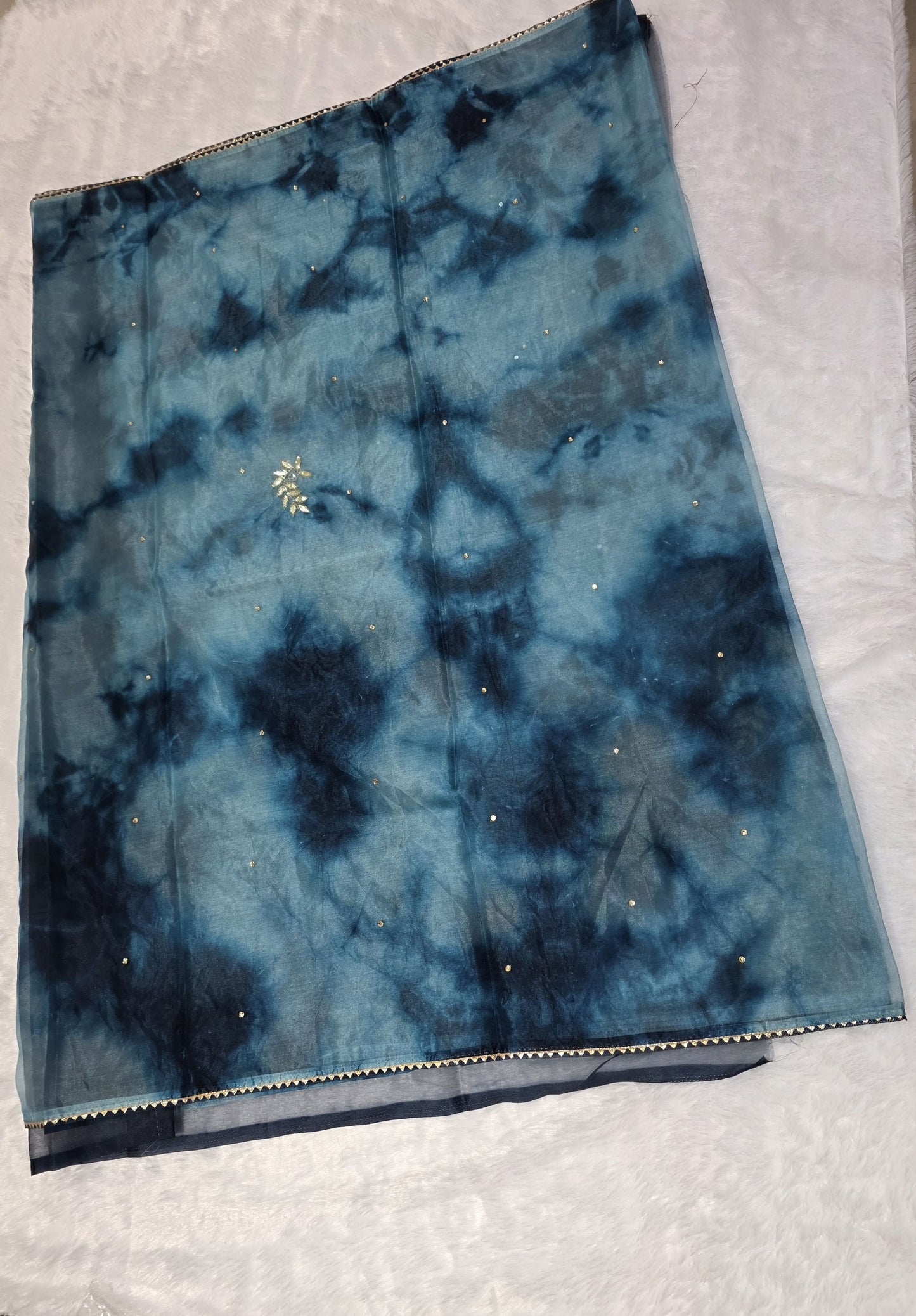 A Gotapatti organza saree crafted with elegant gota patti work, highlighted with scattered sequins for a subtle shimmer. Dual-tone teal and deep blue color palette adds richness and uniqueness. Completed with a matching self blouse.