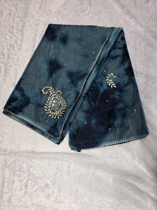 A Gotapatti organza saree crafted with elegant gota patti work, highlighted with scattered sequins for a subtle shimmer. Dual-tone teal and deep blue color palette adds richness and uniqueness. Completed with a matching self blouse.