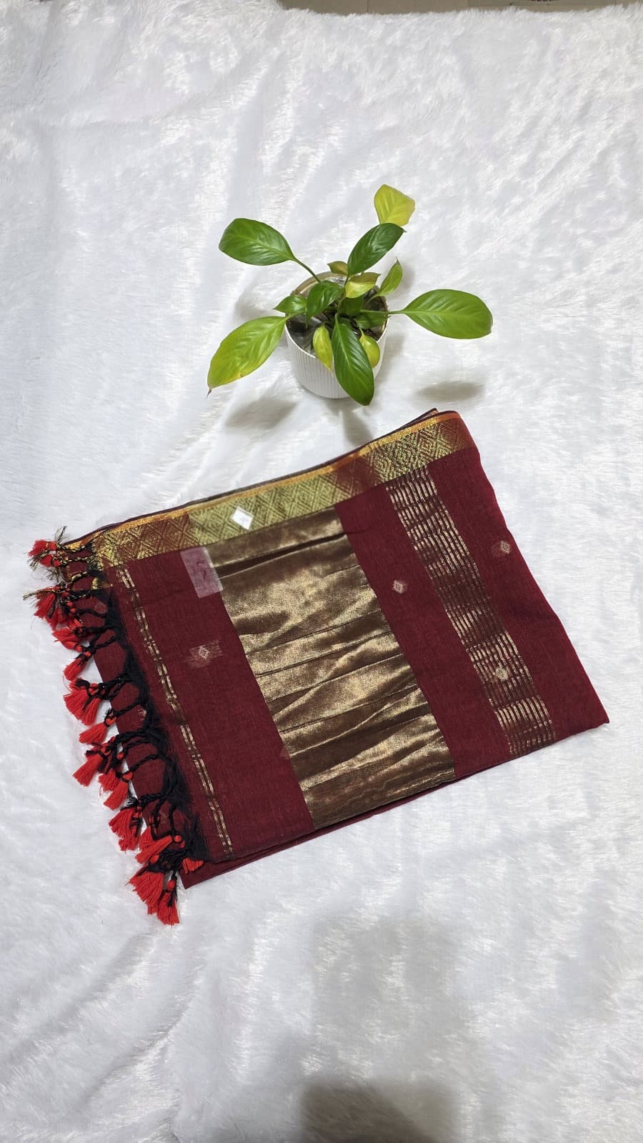 Ethnic maroon cotton saree featuring all-over copper butti design, rich copper zari pallu, and golden border.
