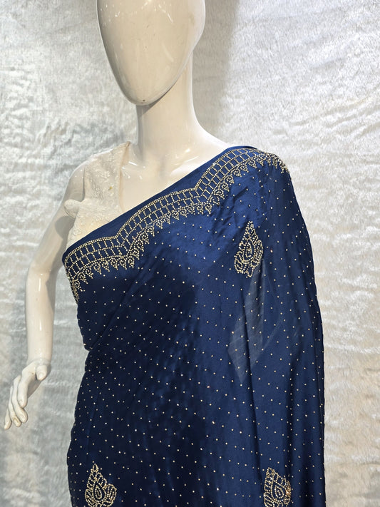 A stunning royal blue pure satin silk saree featuring rich allover stone work buttis that create a glamorous shimmer across the body. The highlight of this saree is its heavy stone-work necklace border, adding a premium designer touch. This saree comes with a matching self royal blue blouse, making it an ideal pick for evening events, parties, and wedding ceremonies where bold elegance stands out.