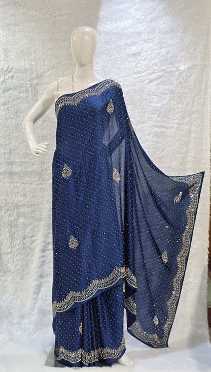 A stunning royal blue pure satin silk saree featuring rich allover stone work buttis that create a glamorous shimmer across the body. The highlight of this saree is its heavy stone-work necklace border, adding a premium designer touch. This saree comes with a matching self royal blue blouse, making it an ideal pick for evening events, parties, and wedding ceremonies where bold elegance stands out.