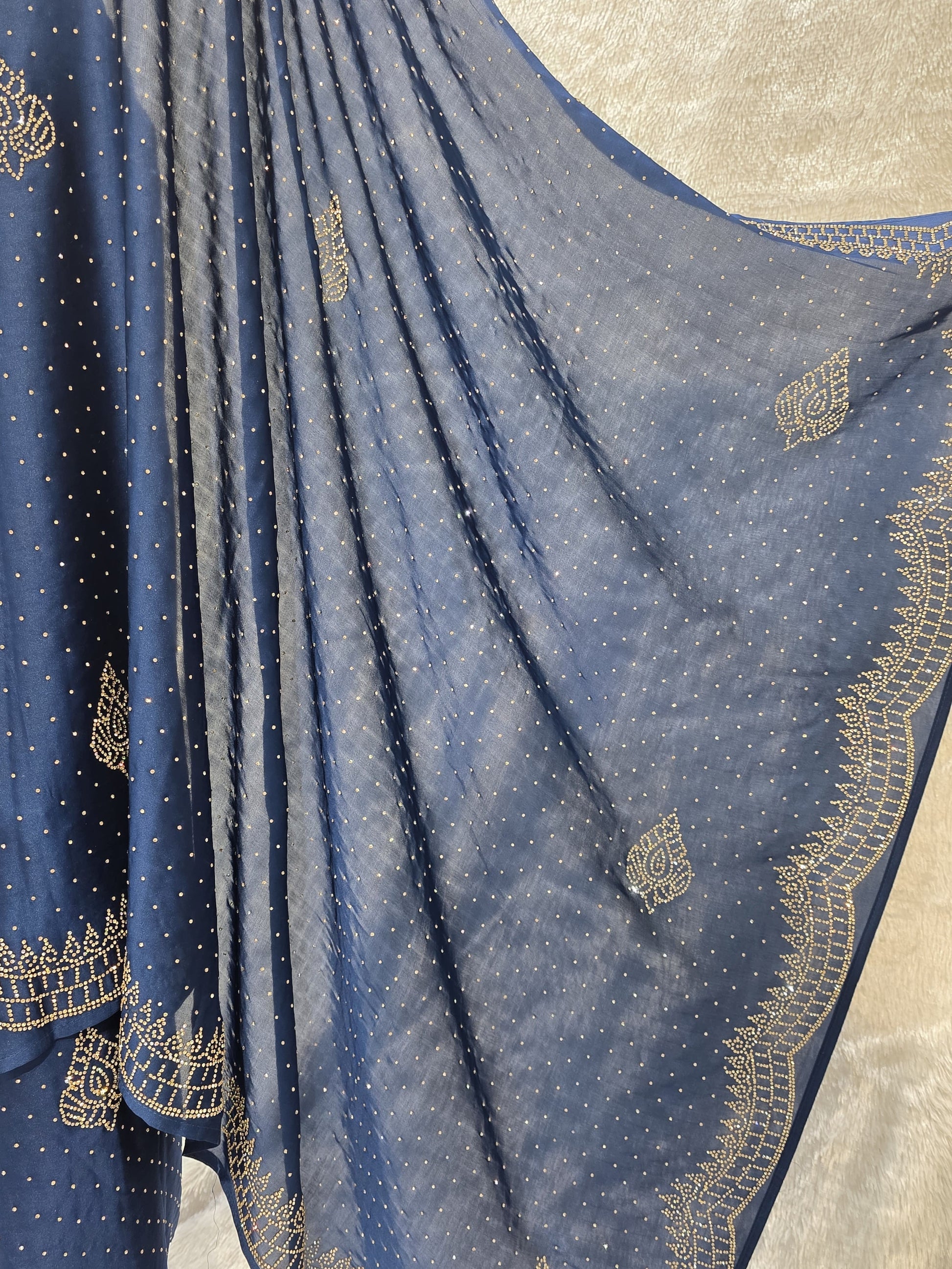 A stunning royal blue pure satin silk saree featuring rich allover stone work buttis that create a glamorous shimmer across the body. The highlight of this saree is its heavy stone-work necklace border, adding a premium designer touch. This saree comes with a matching self royal blue blouse, making it an ideal pick for evening events, parties, and wedding ceremonies where bold elegance stands out.
