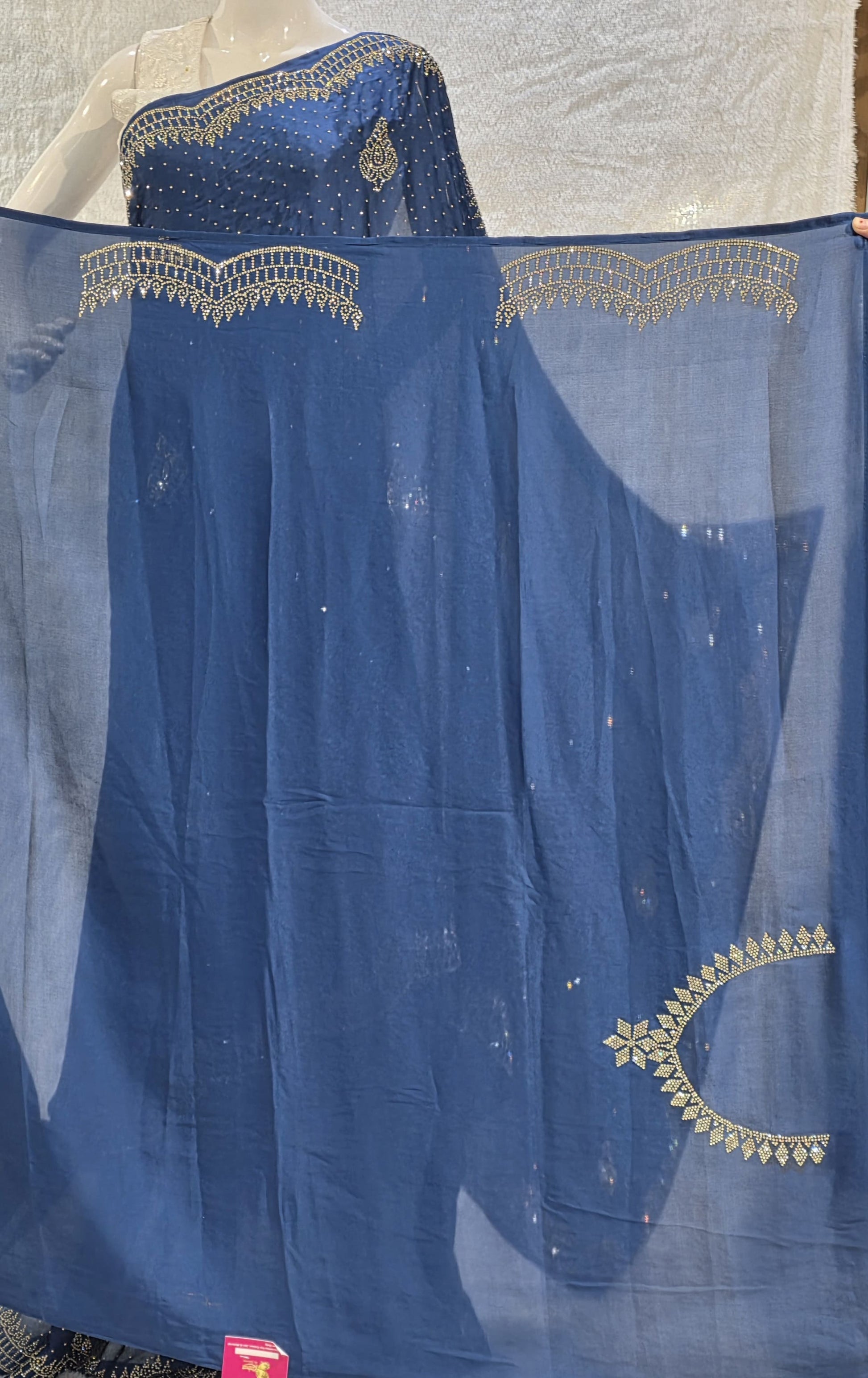 A stunning royal blue pure satin silk saree featuring rich allover stone work buttis that create a glamorous shimmer across the body. The highlight of this saree is its heavy stone-work necklace border, adding a premium designer touch. This saree comes with a matching self royal blue blouse, making it an ideal pick for evening events, parties, and wedding ceremonies where bold elegance stands out.