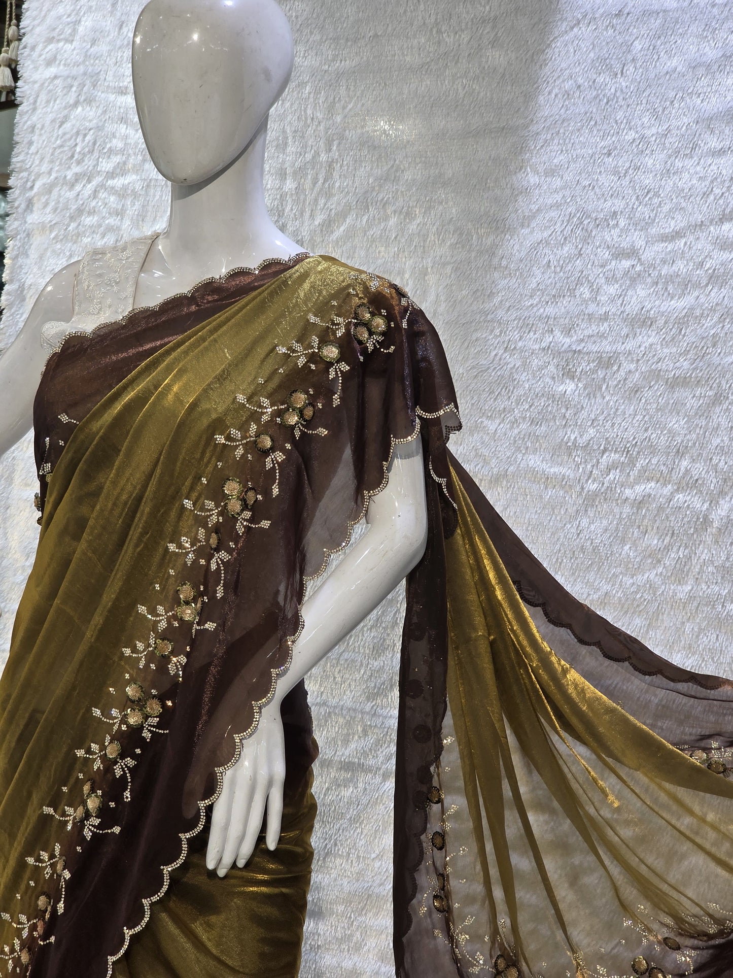 This premium copper pure satin silk saree features a stylish plain body complemented by a beautifully crafted border with floral stone work and tikali detailing. The added necklace border design enhances its regal appeal. Paired with a contrast chocolate-brown blouse, this saree carries a sophisticated modern-traditional blend, perfect for festive occasions and elegant evening wear.