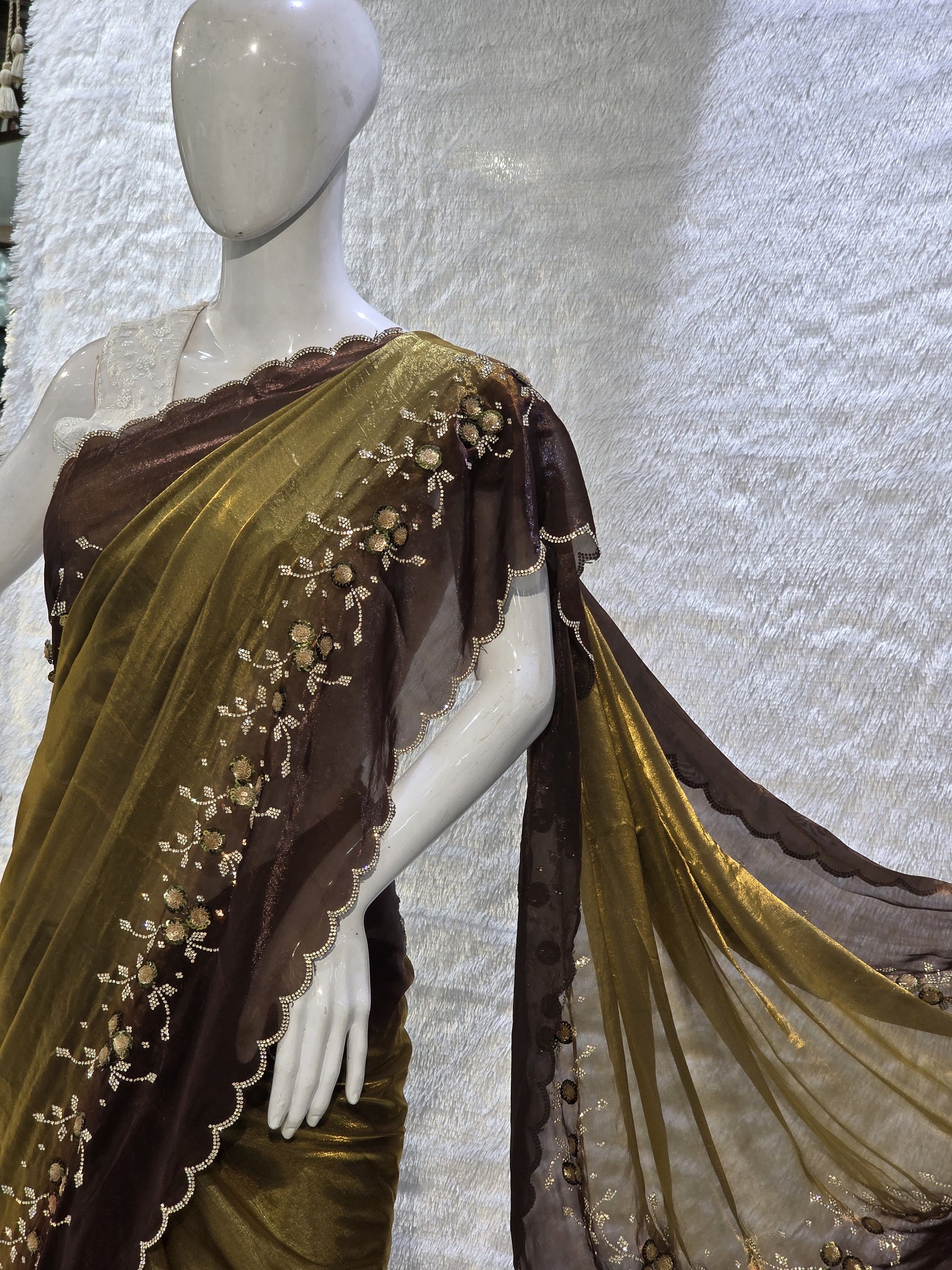 This premium copper pure satin silk saree features a stylish plain body complemented by a beautifully crafted border with floral stone work and tikali detailing. The added necklace border design enhances its regal appeal. Paired with a contrast chocolate-brown blouse, this saree carries a sophisticated modern-traditional blend, perfect for festive occasions and elegant evening wear.