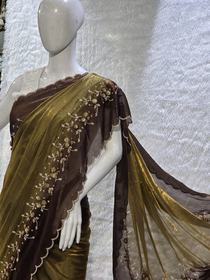 This premium copper pure satin silk saree features a stylish plain body complemented by a beautifully crafted border with floral stone work and tikali detailing. The added necklace border design enhances its regal appeal. Paired with a contrast chocolate-brown blouse, this saree carries a sophisticated modern-traditional blend, perfect for festive occasions and elegant evening wear.
