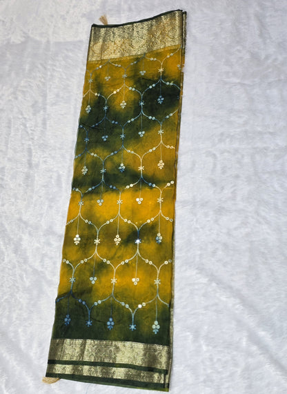 An intricate organza gotapatti  saree featuring allover shimmering accents, sequins/mirror-like detailing and traditional gota patti lace border. Lightweight yet festive, perfect for family occasions. Comes with a self blouse in matching tone.