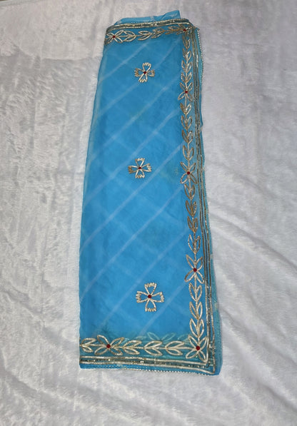 This sky-blue organza Gota pattivsaree showcases a soothing leheriya design enhanced with gold gota patti border detailing. Ideal for daytime events and celebrations. Paired with a coordinated self blouse.