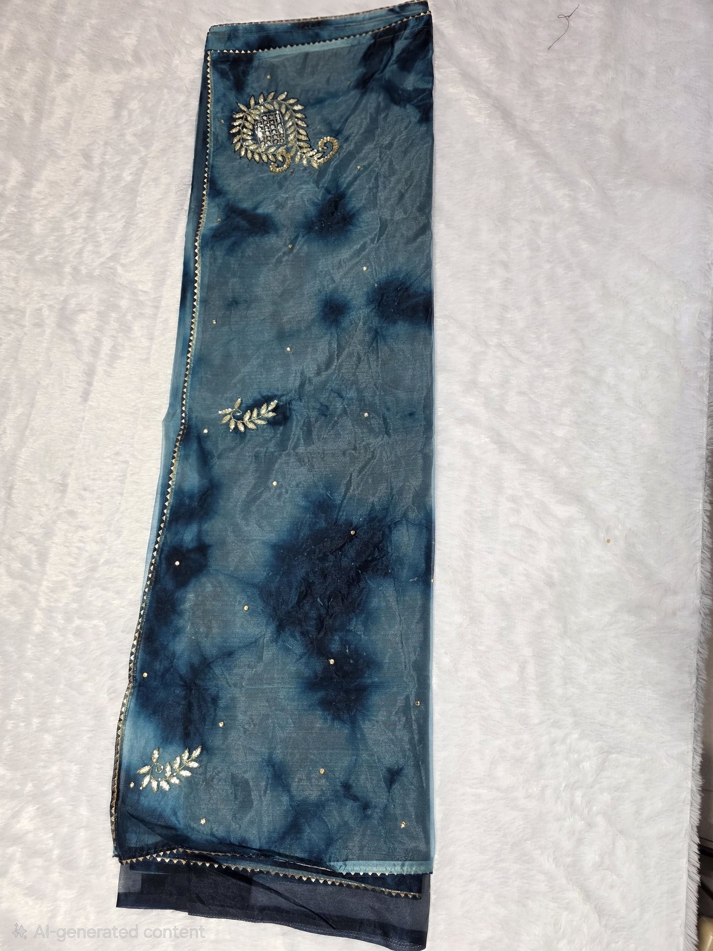 A Gotapatti  organza saree crafted with elegant gota patti work, highlighted with scattered sequins for a subtle shimmer. Dual-tone teal and deep blue color palette adds richness and uniqueness. Completed with a matching self blouse.