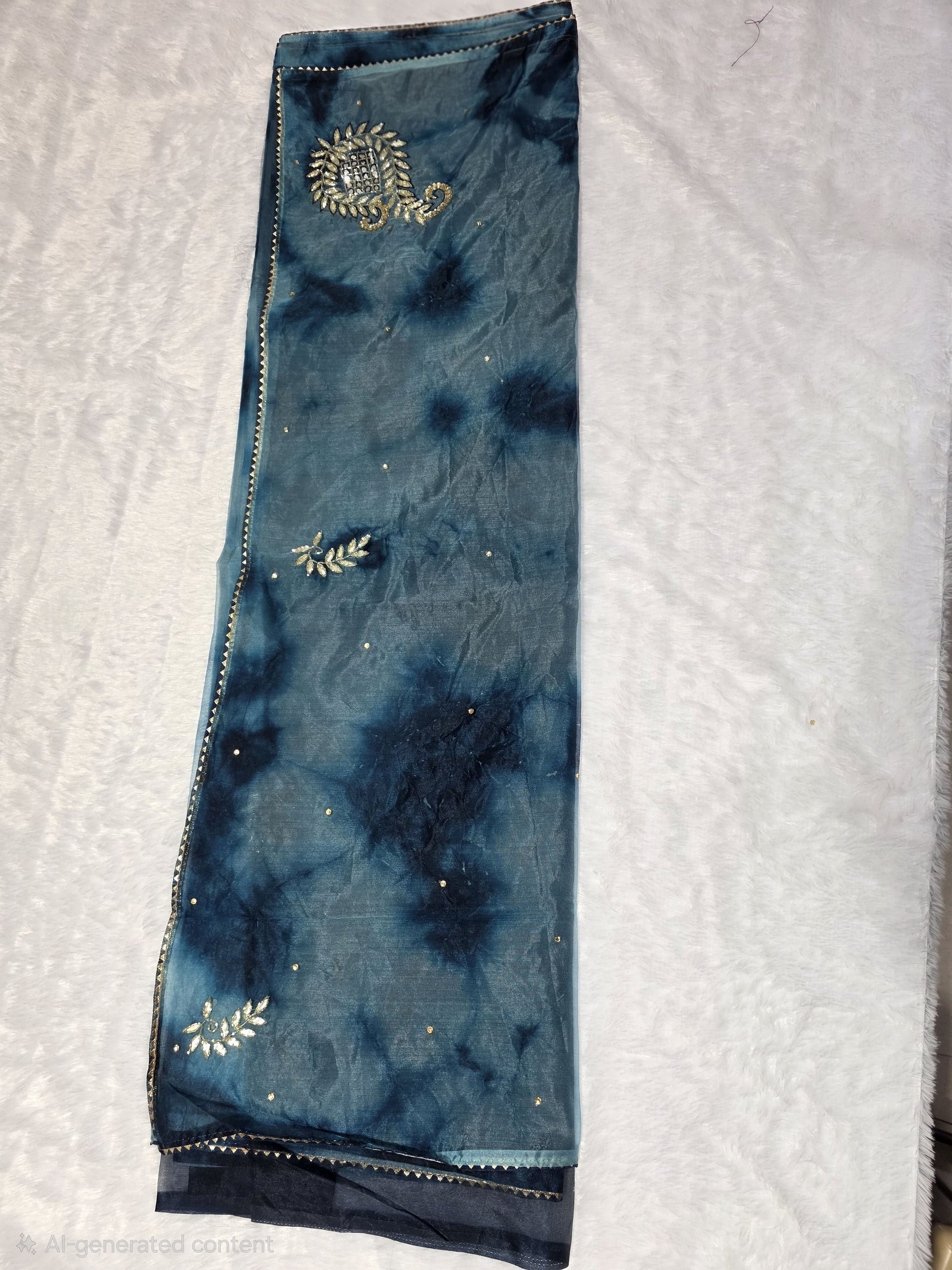 A Gotapatti  organza saree crafted with elegant gota patti work, highlighted with scattered sequins for a subtle shimmer. Dual-tone teal and deep blue color palette adds richness and uniqueness. Completed with a matching self blouse.