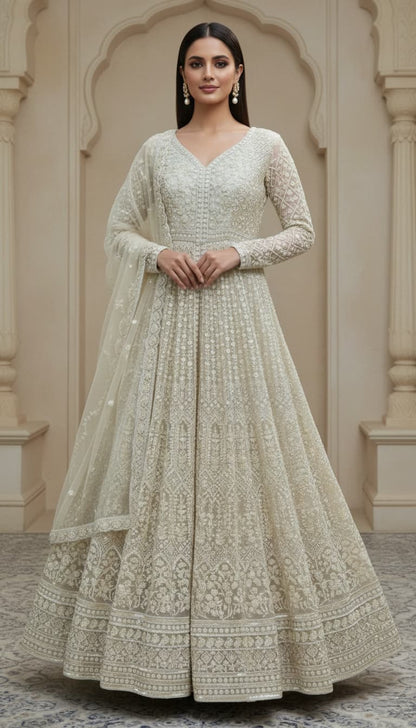  ivory Anarkali crafted in delicate net fabric and adorned with intricate hand embroidery. Designed with a flattering V-neckline and a fitted bodice, the silhouette flows into a beautifully flared floor-length hem, creating an effortlessly regal look. 