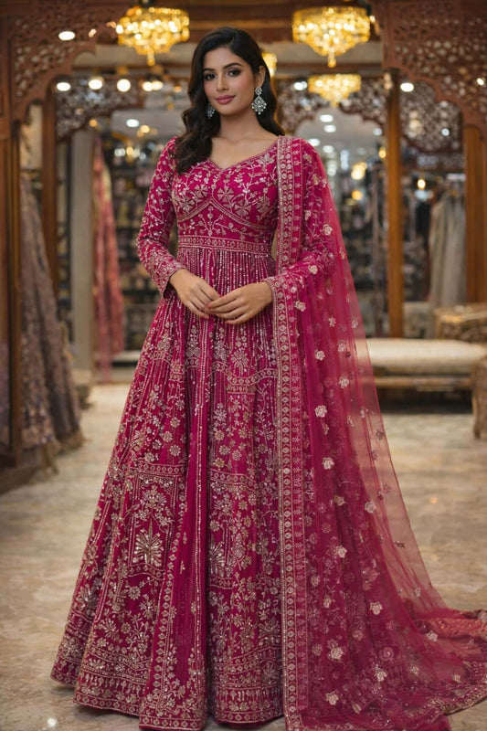  this stunning rani pink Anarkali gown crafted in delicate net fabric and adorned with intricate sequin and bead embroidery. Designed with a flattering V-neckline and fitted bodice, the silhouette flows into a beautifully flared floor-length hem for a regal and graceful look. 
