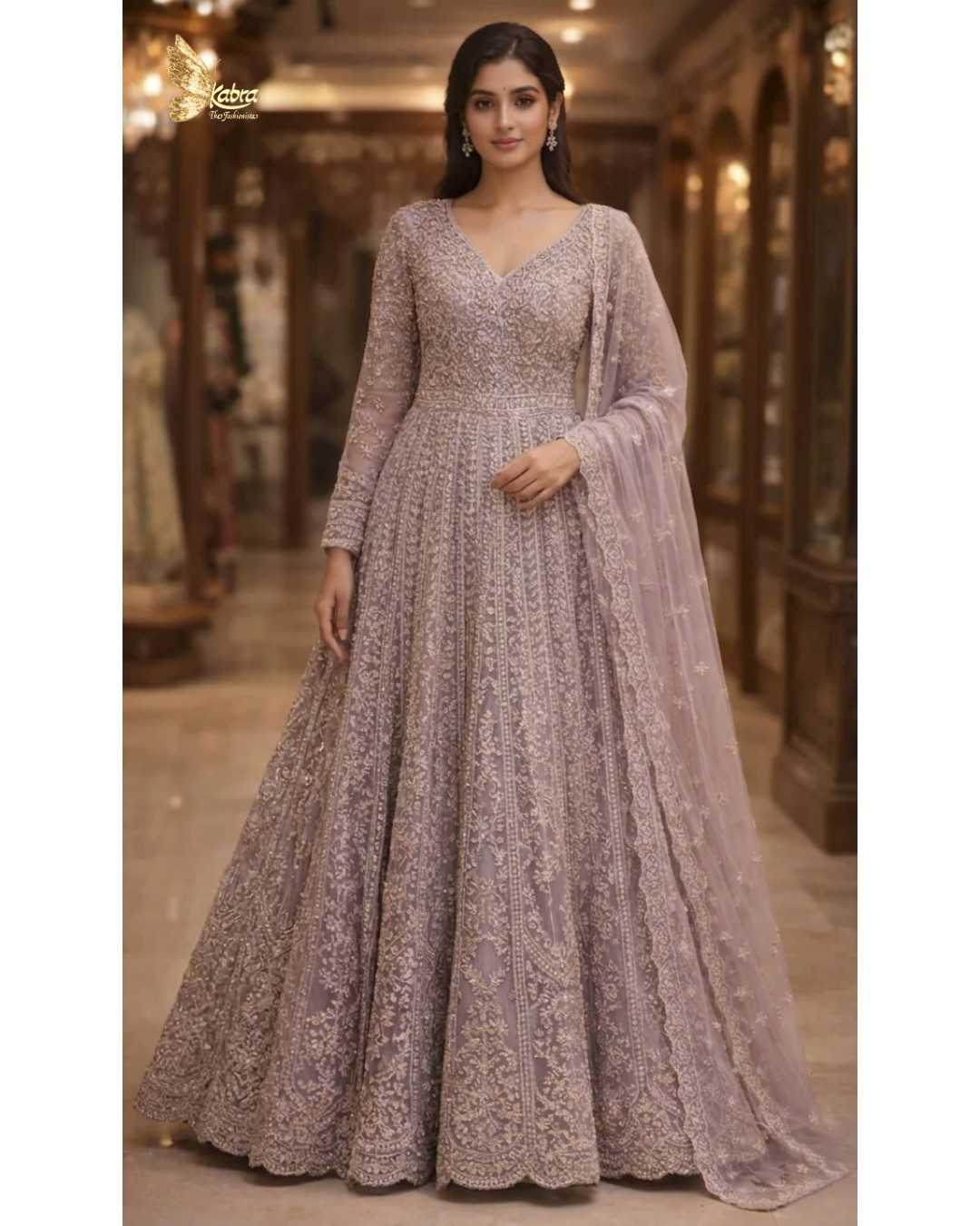 this exquisite dusty lavender front cut Anarkali crafted in delicate net fabric and adorned with intricate zari, sequin, and bead embroidery. Designed with a flattering V-neckline and a fitted bodice, the silhouette flows into a beautifully flared floor-length hem with a graceful center slit, creating a soft yet regal statement.
