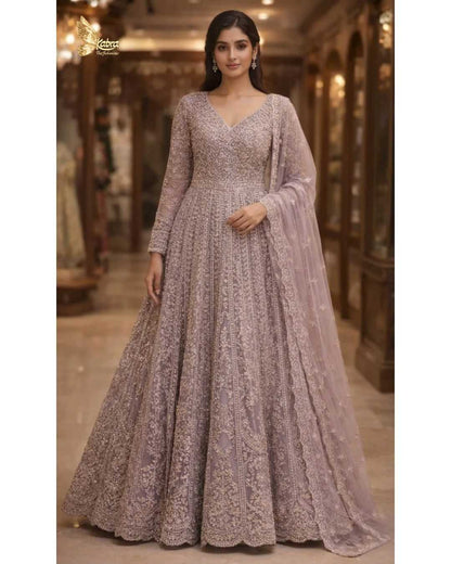 this exquisite dusty lavender front cut Anarkali crafted in delicate net fabric and adorned with intricate zari, sequin, and bead embroidery. Designed with a flattering V-neckline and a fitted bodice, the silhouette flows into a beautifully flared floor-length hem with a graceful center slit, creating a soft yet regal statement.
