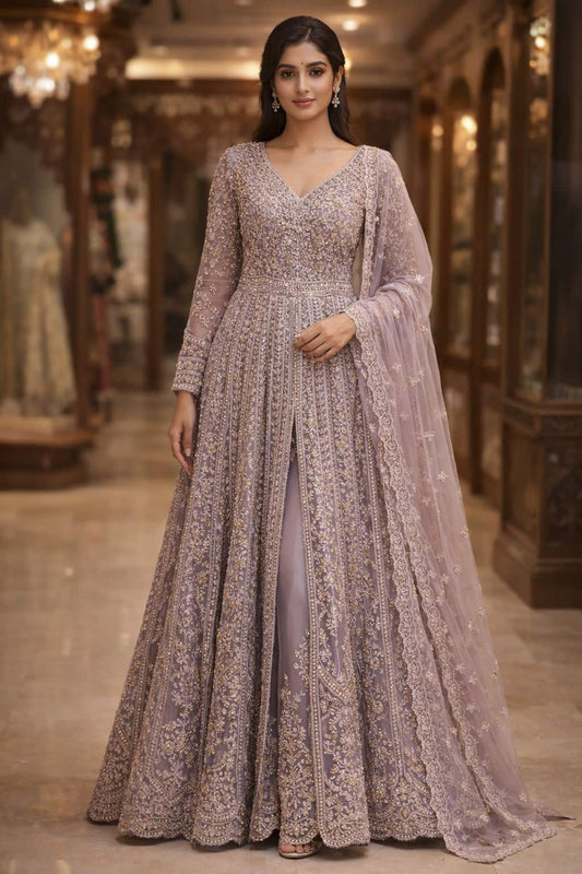 this exquisite dusty lavender front cut Anarkali crafted in delicate net fabric and adorned with intricate zari, sequin, and bead embroidery. Designed with a flattering V-neckline and a fitted bodice, the silhouette flows into a beautifully flared floor-length hem with a graceful center slit, creating a soft yet regal statement.