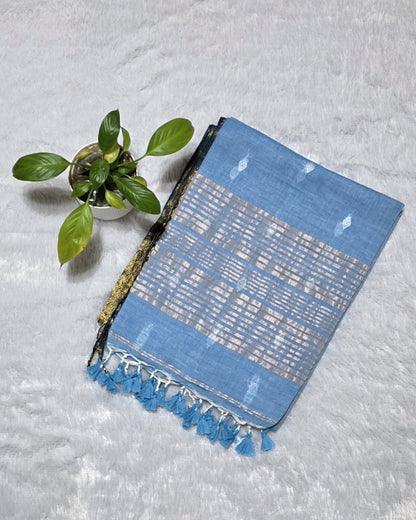 Traditional sky blue cotton saree adorned with silver butti pattern, golden line detailing on the pallu, and golden border.