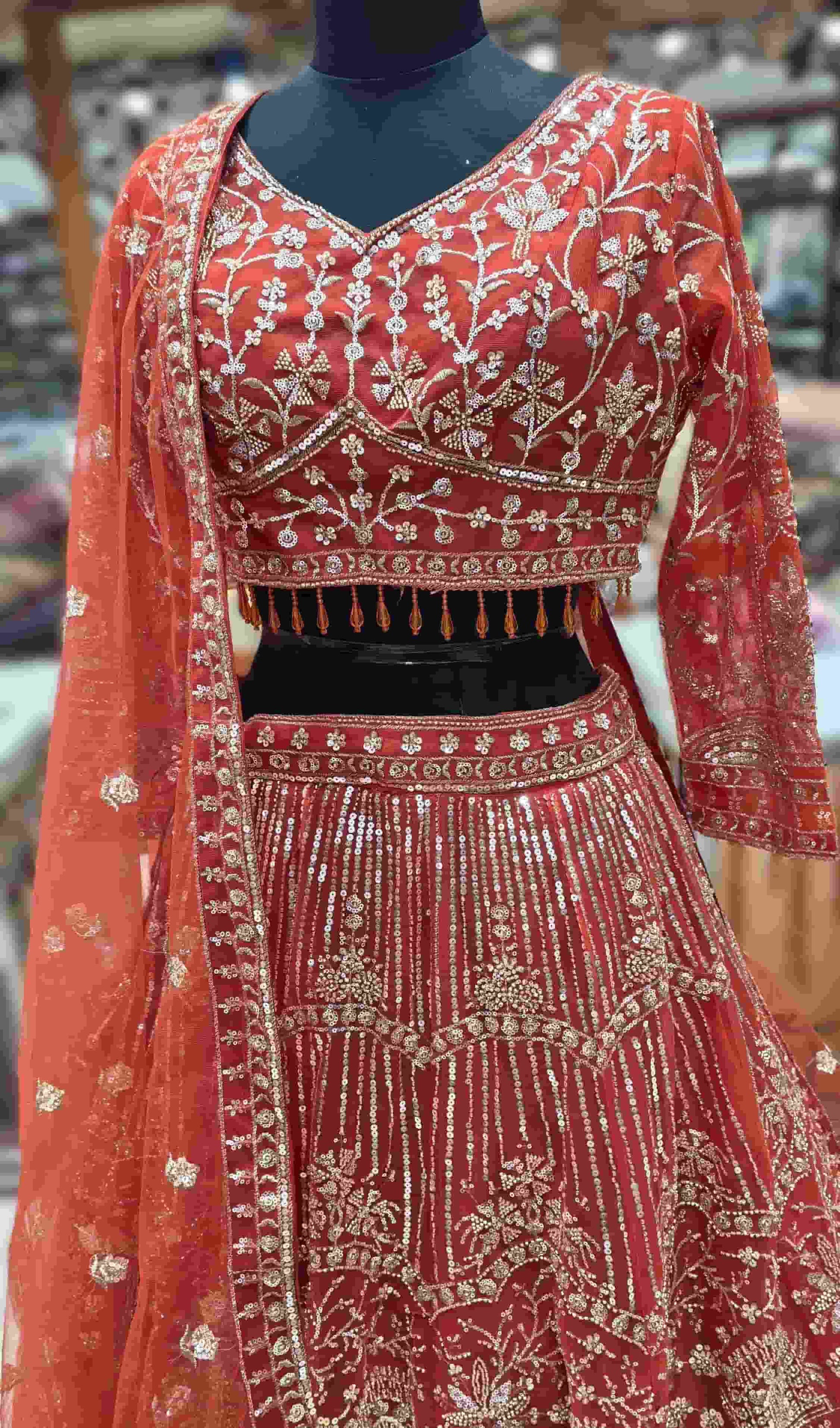 Close-up of rust orange V-neck blouse with floral sequin embroidery and sheer sleeves.